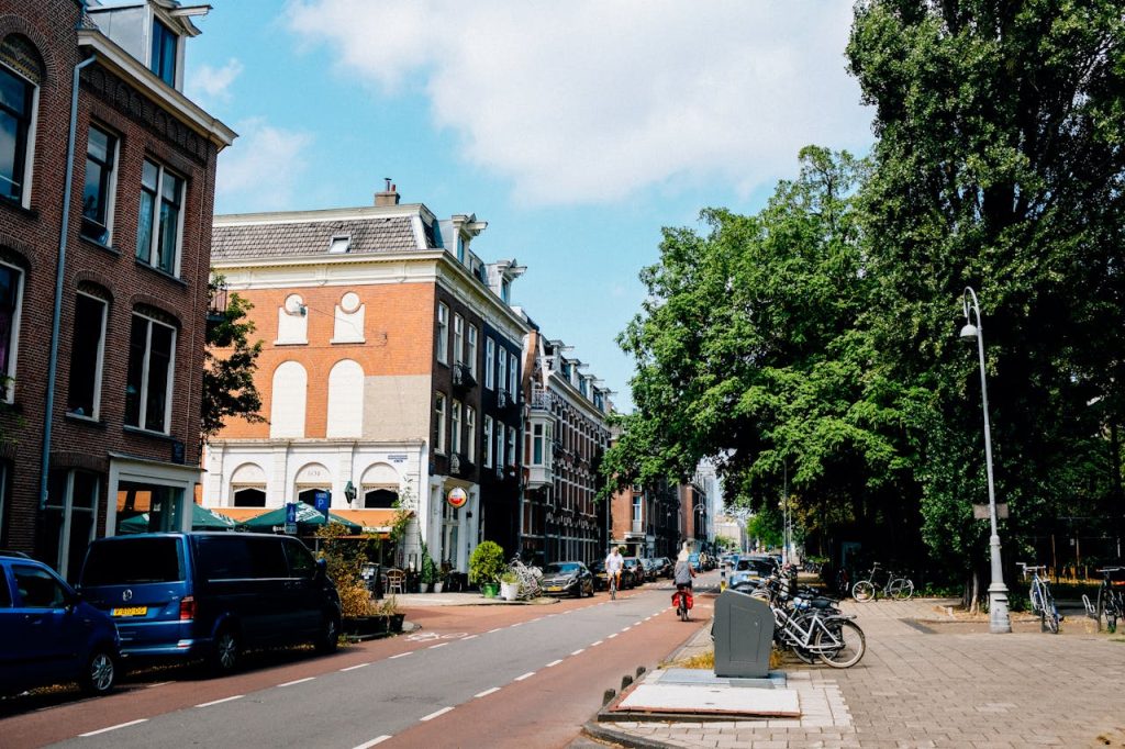 A picturesque street in Amsterdam featuring classic architecture, bicycles, and parked cars under a clear sky.